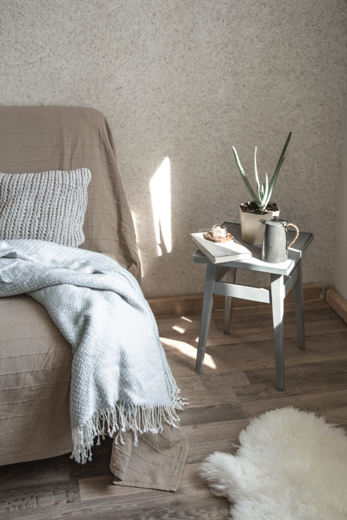 Vaalea sohva, jolla on koristetyynyjä ja viltti, kodikkaasti sisustetussa olohuoneessa.