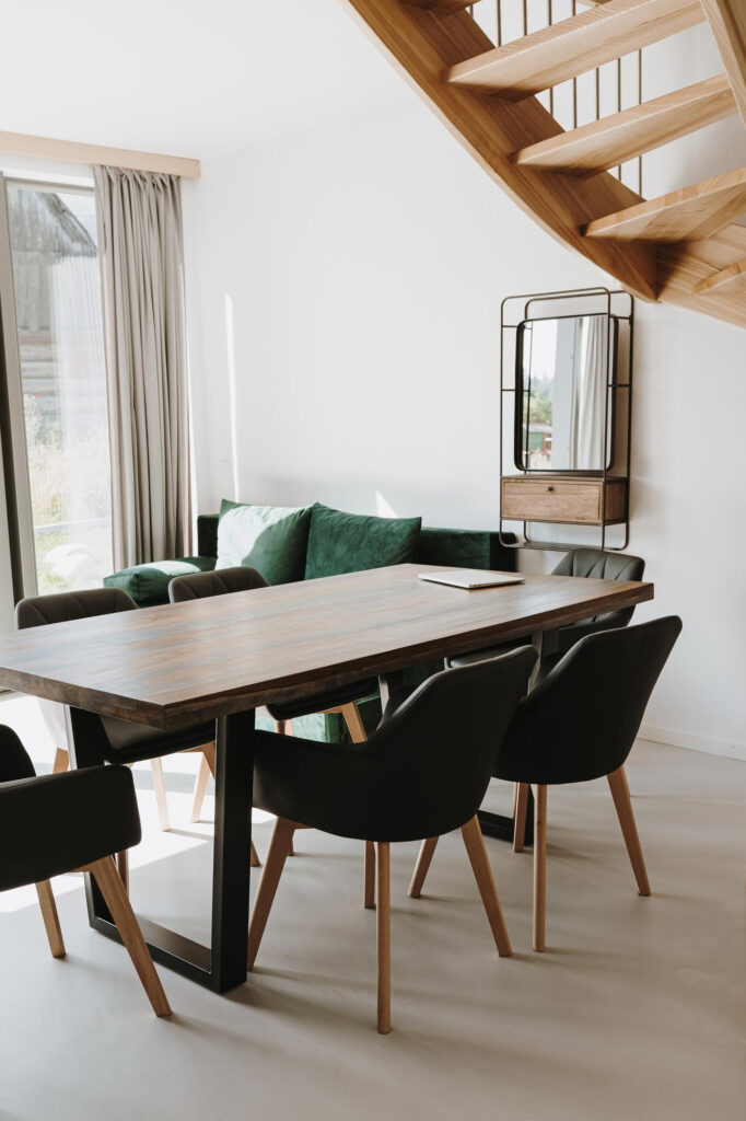 Moderni ruokailutila, jossa on tumma puupöytä ja mustia tuoleja. Taustalla näkyy puinen portaikko.