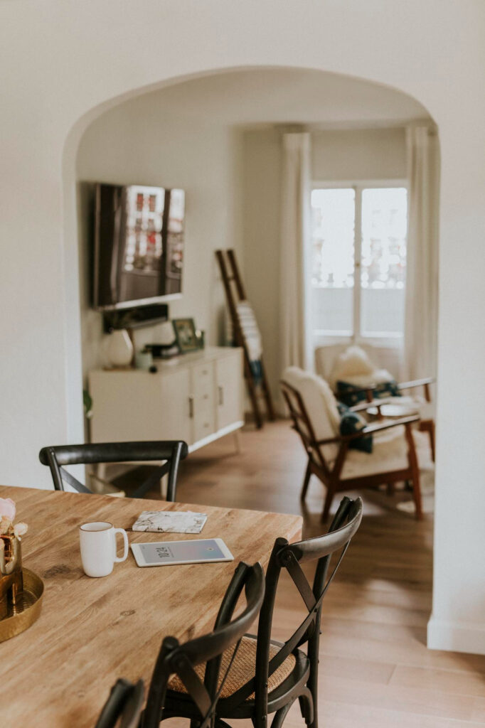 Näkymä puiselta ruokapöydältä kaarioven kautta valoisaan olohuoneeseen.