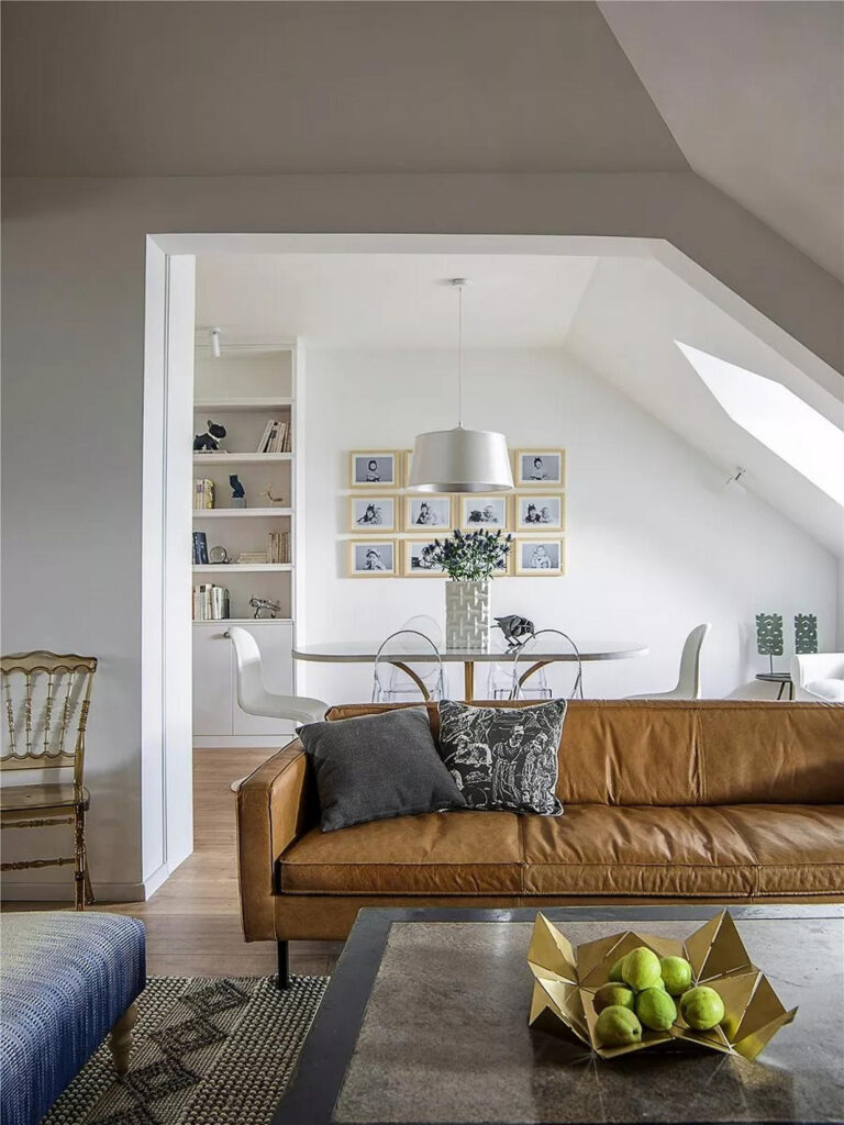 Ruskea nahkasohva olohuoneessa, josta on näkymä valoisaan ruokailutilaan vinokaton alla.