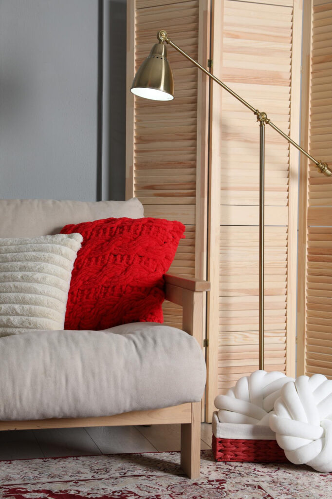 Olohuoneen nurkkaus, jossa on sohva, messinkinen lattiavalaisin ja puinen sermi.